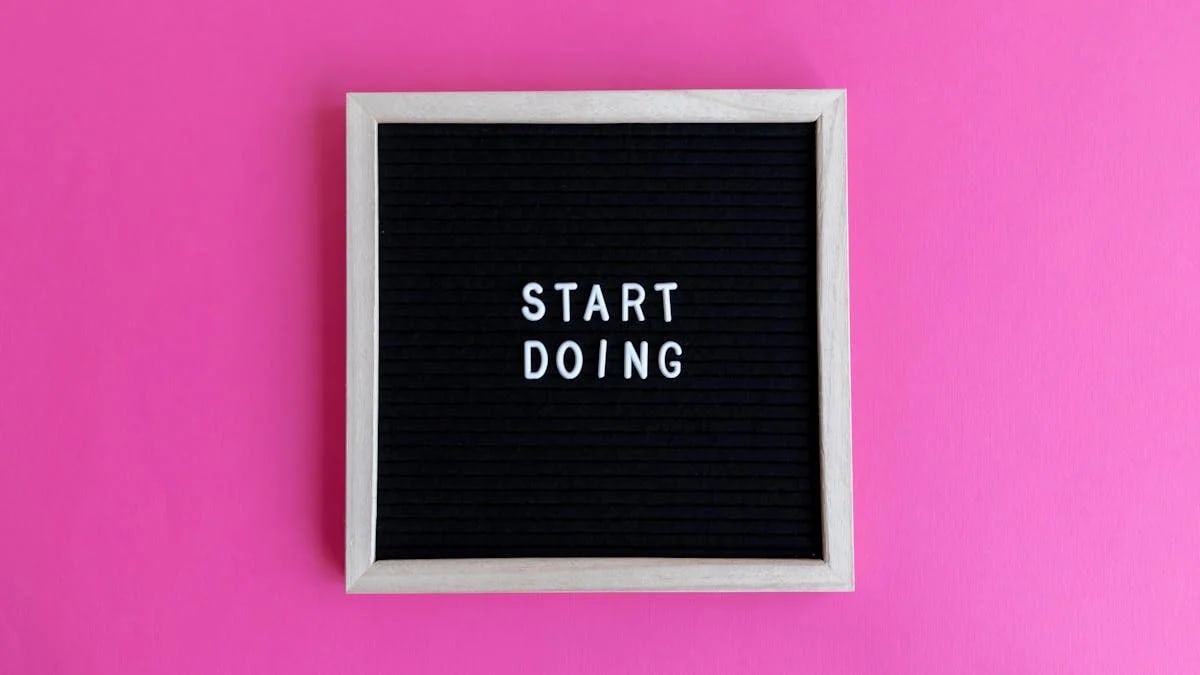 Black letter board with 'Start Doing' motivational text on bright pink background.